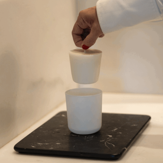 A hand lowering a new wax refill into a white Waks candle glass